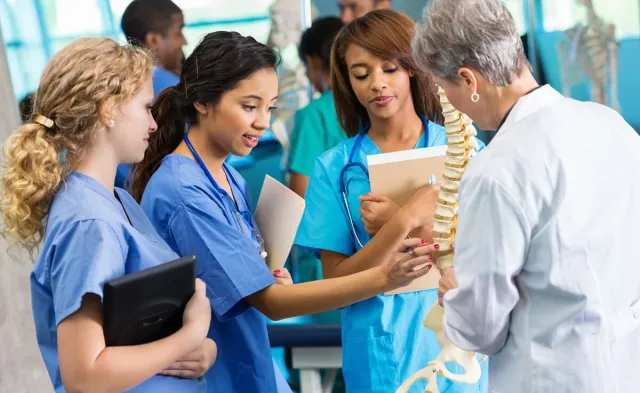 Three nursing students learning skeletal structure from nurse teacher