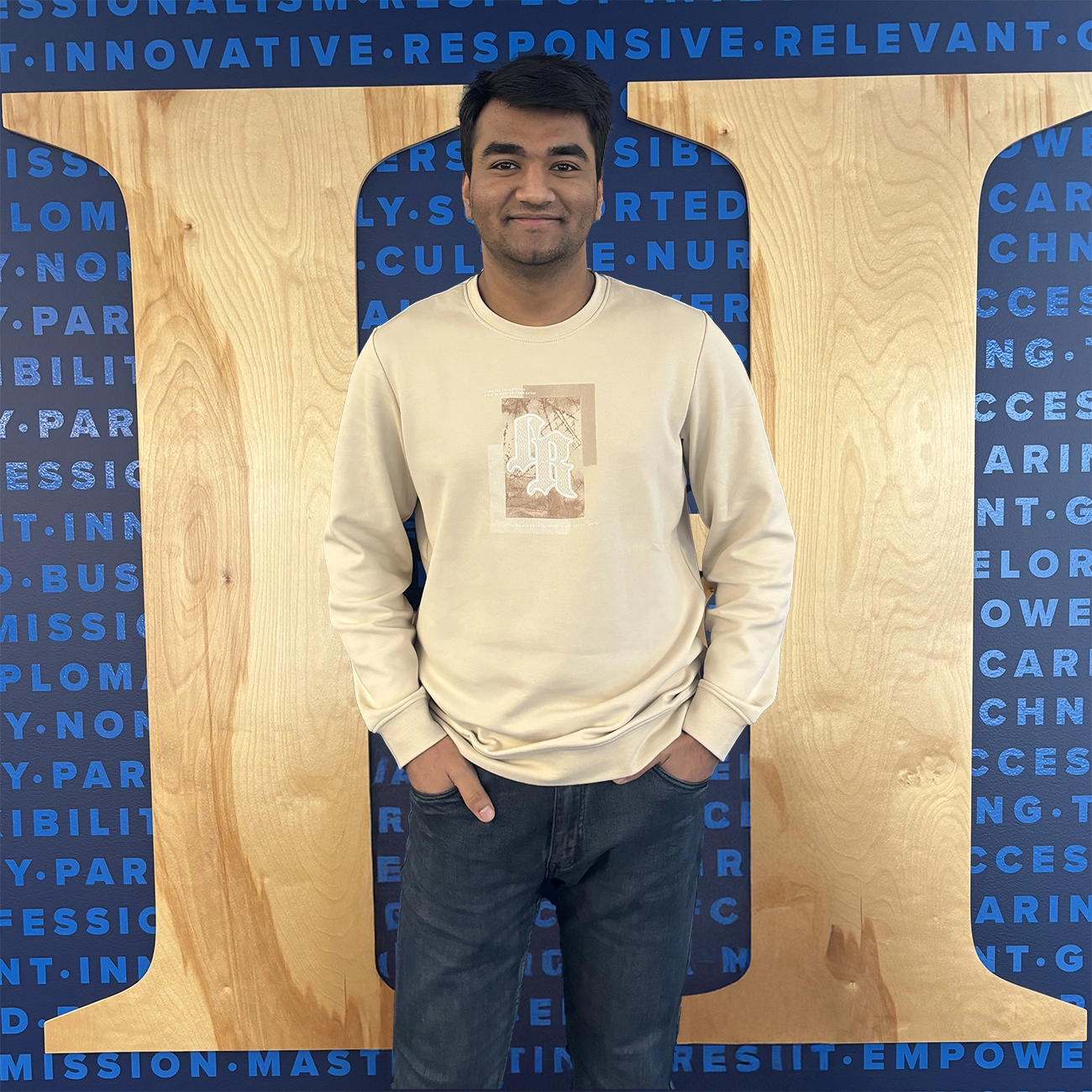 International student smiling and posing in front of a Herzing University wall with the university’s logo and motivational words in the background.