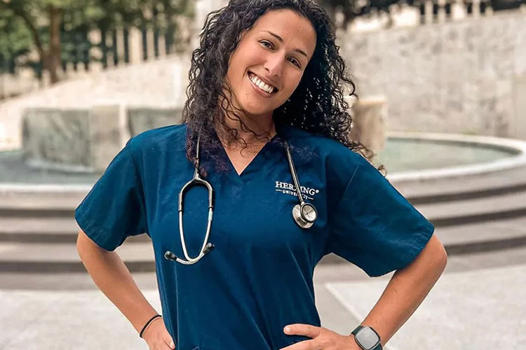 Herzing online BSN student in blue scrubs smiling with hands on hips in courtyard