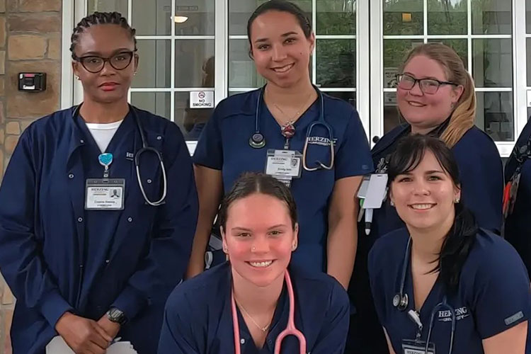 Herzing online associate in nursing students wearing blue scrubs smiling during intensive experience