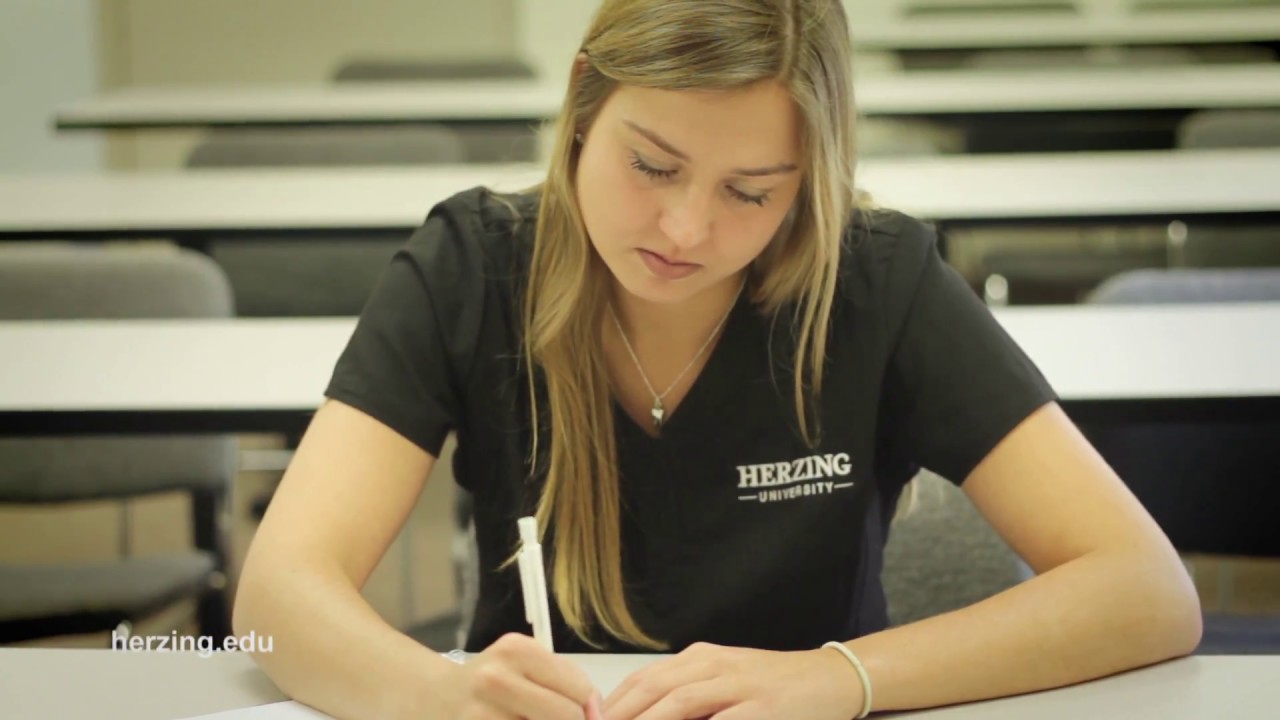 Herzing dental hygiene student in scrubs taking notes during class