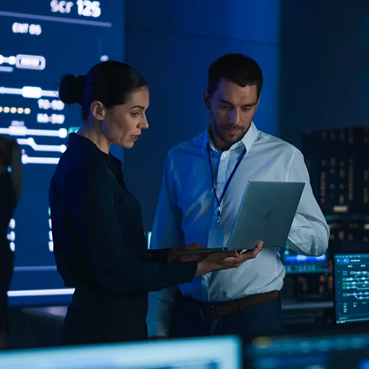 Two cybersecurity managers discussing strategy in office referencing information on laptop