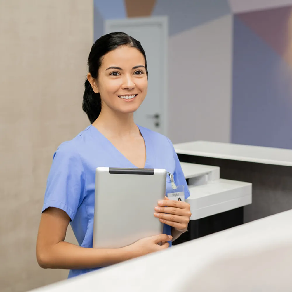 Medical assistant in front office holding tablet and smiling with patient
