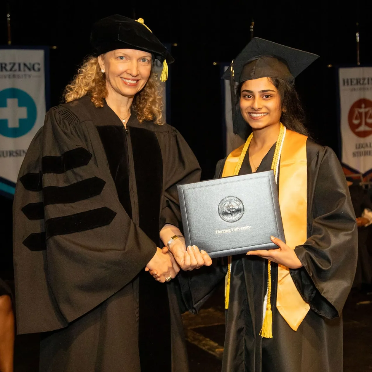 Herzing University graduation ceremony, professor shaking hands with a graduate holding their diploma.