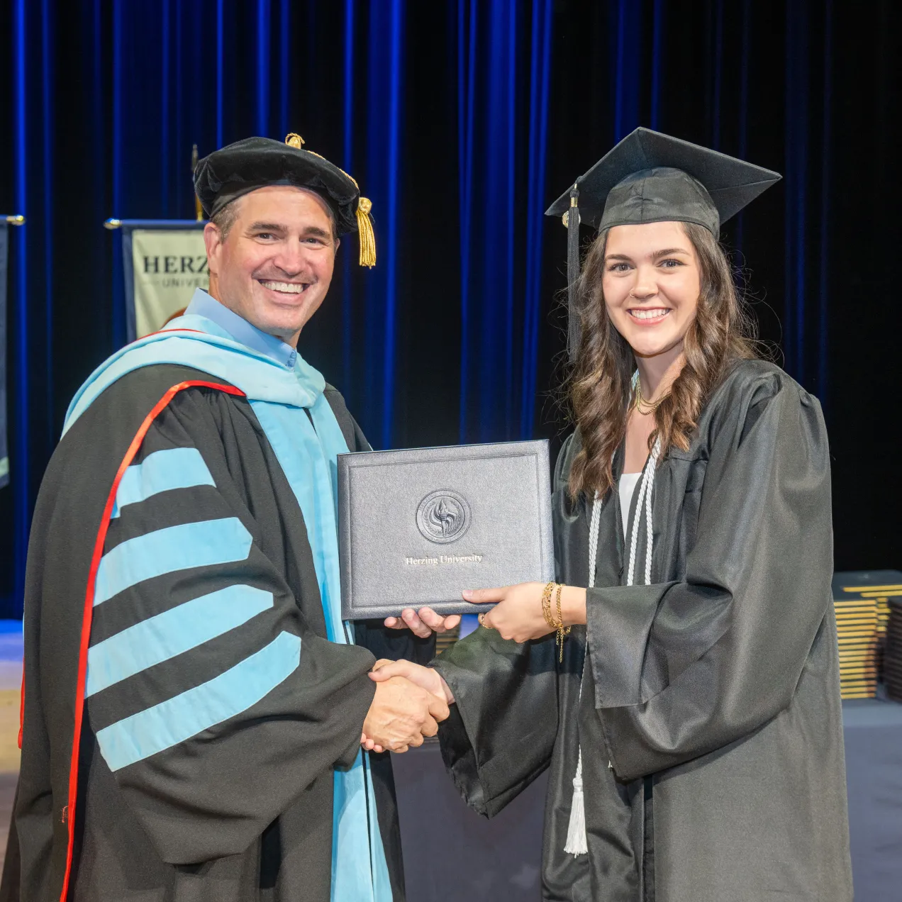 A Herzing University graduate smiling and receiving her diploma during a commencement ceremony, celebrating her academic achievement.