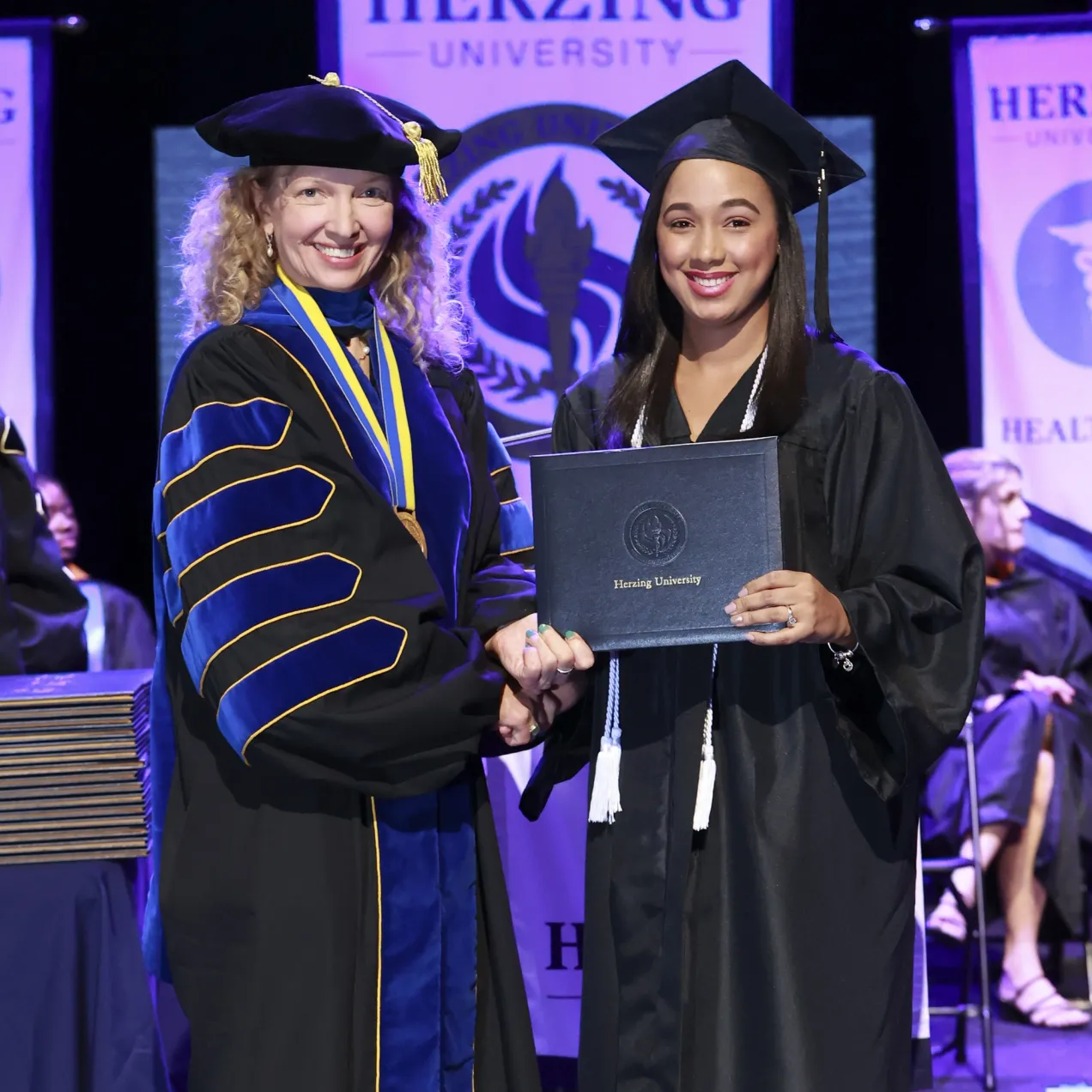 Herzing University graduate receiving their diploma on stage during a commencement ceremony.