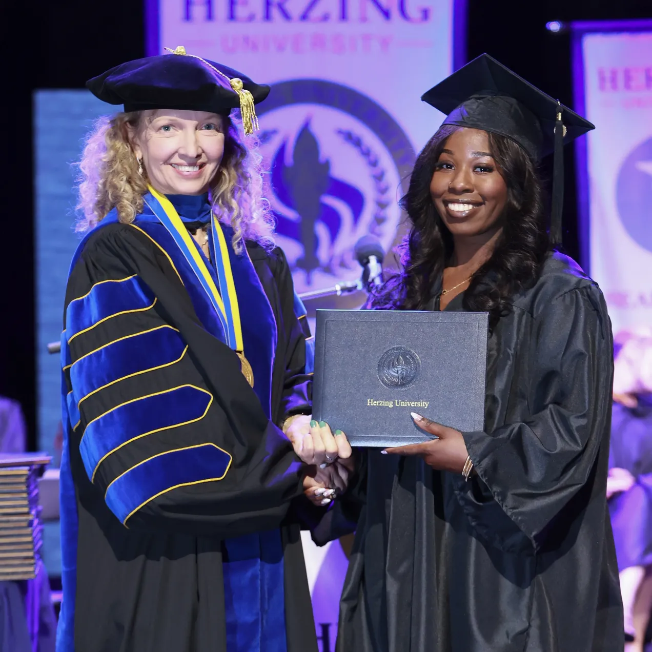 Graduate receiving a diploma on stage during a Herzing University commencement ceremony in Healthcare Administration.