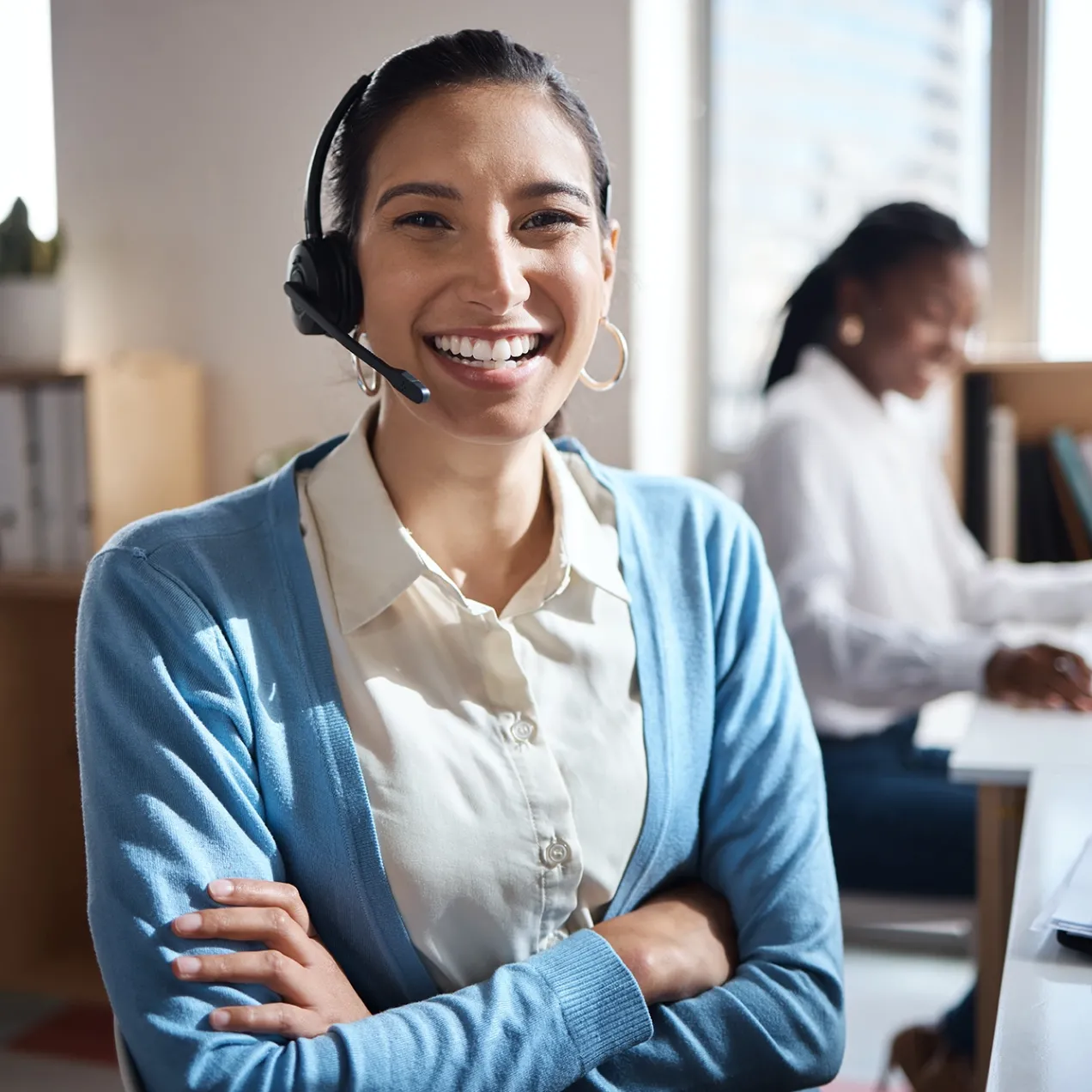 Friendly female receptionist wearing a headset, assisting a caller while working at a front desk in a medical or office setting.