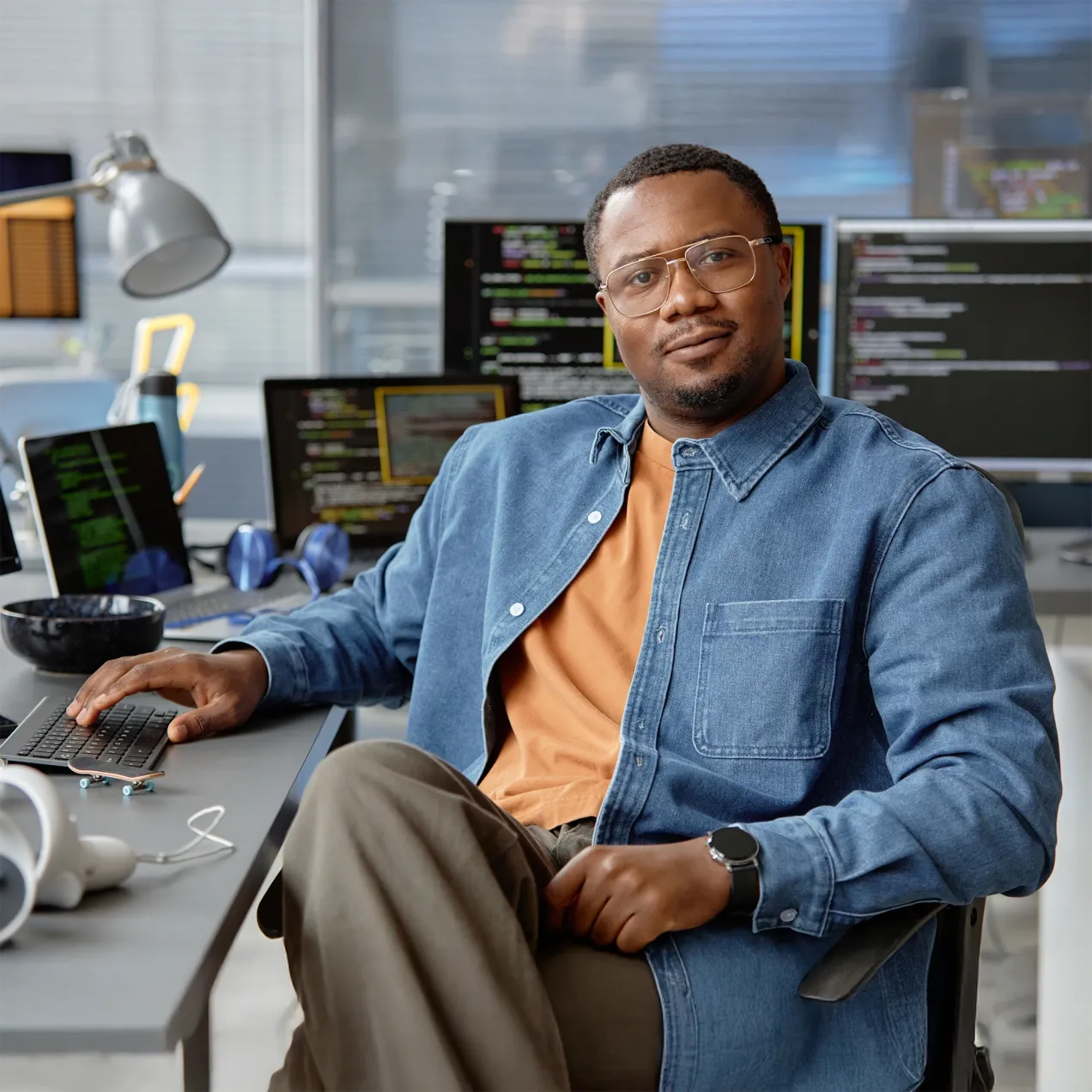 A confident cybersecurity professional sitting at a desk in a modern office, surrounded by multiple screens displaying lines of code, representing the expertise and practical skills gained through Herzing University’s graduate-level cybersecurity program.