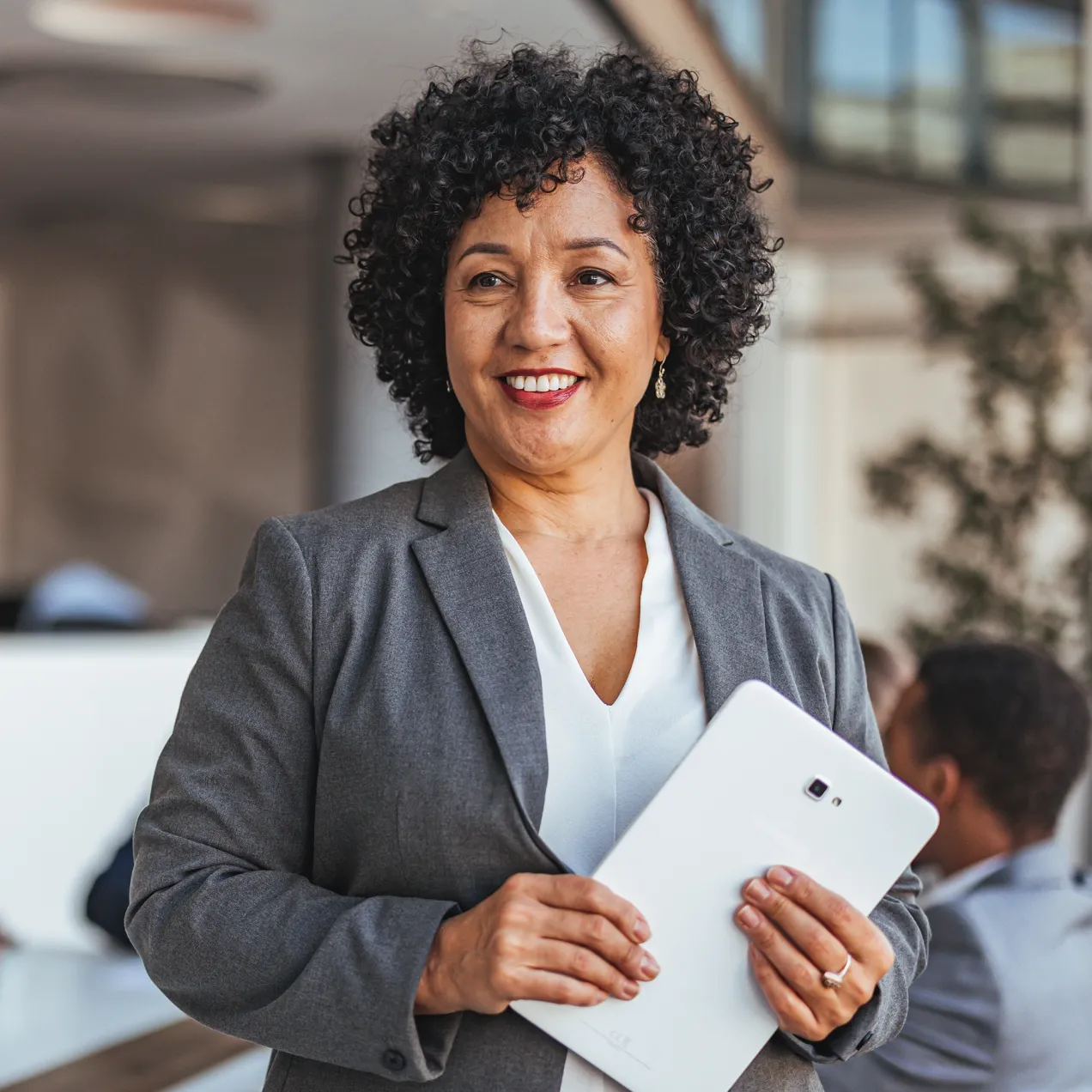 Professional woman in a business suit holding a tablet, smiling confidently in a modern office setting.