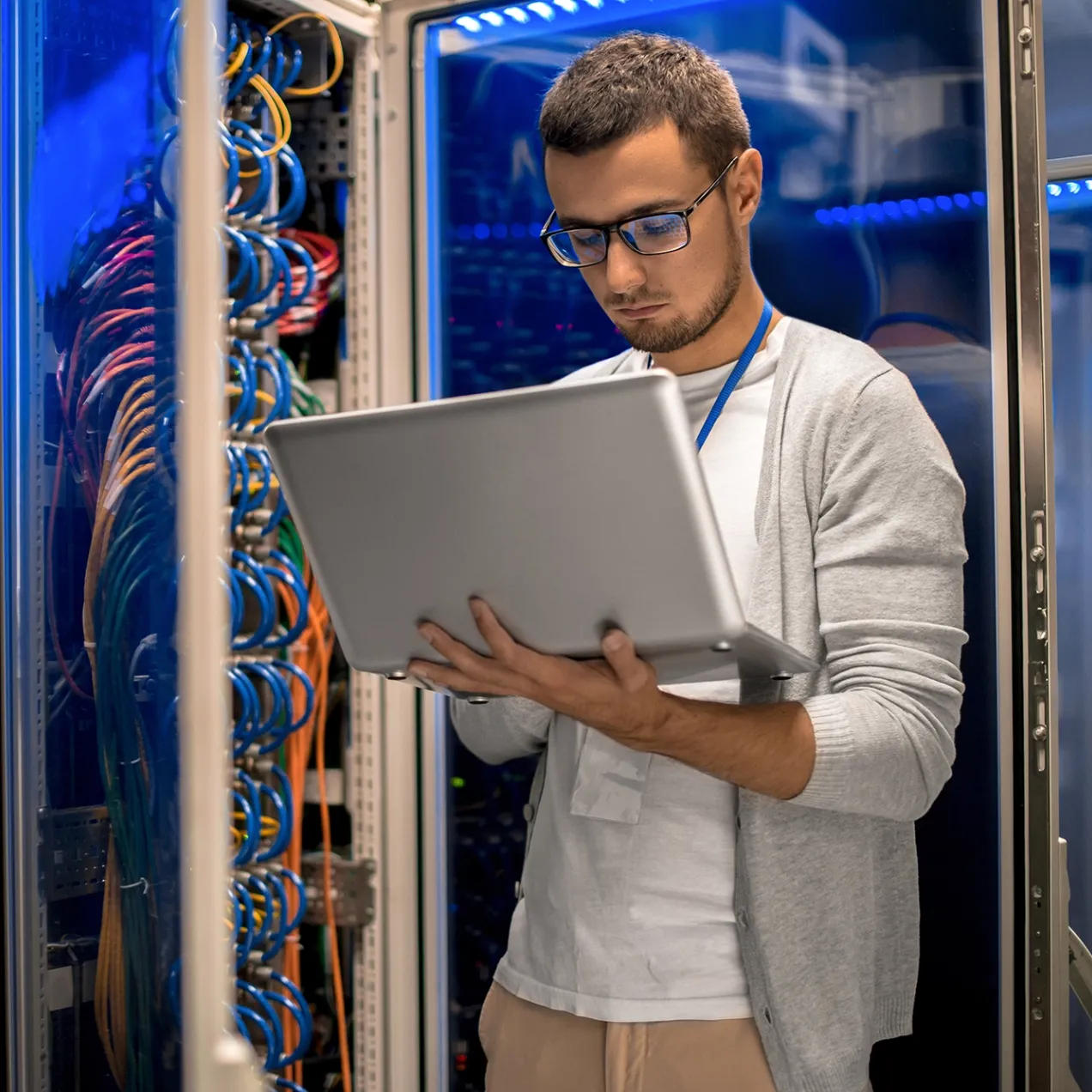 IT professional working on a laptop in a server room, managing network infrastructure and cybersecurity in the Information Technology program.