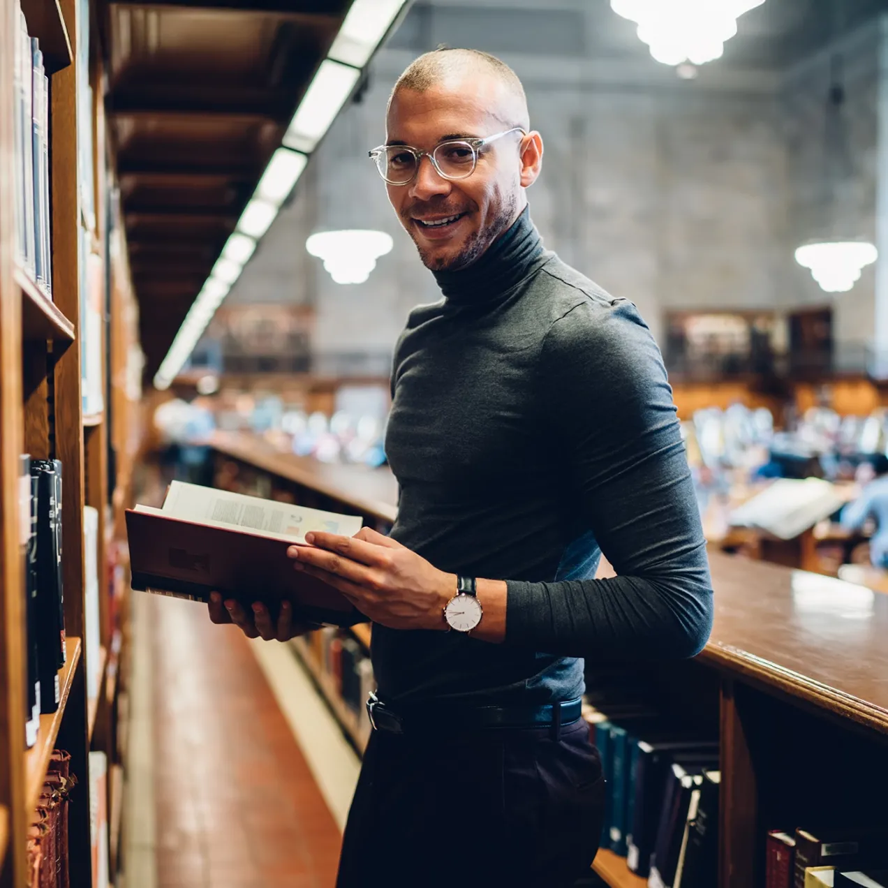 A confident man in a modern law library holding a legal textbook, representing students in the Legal Studies program.