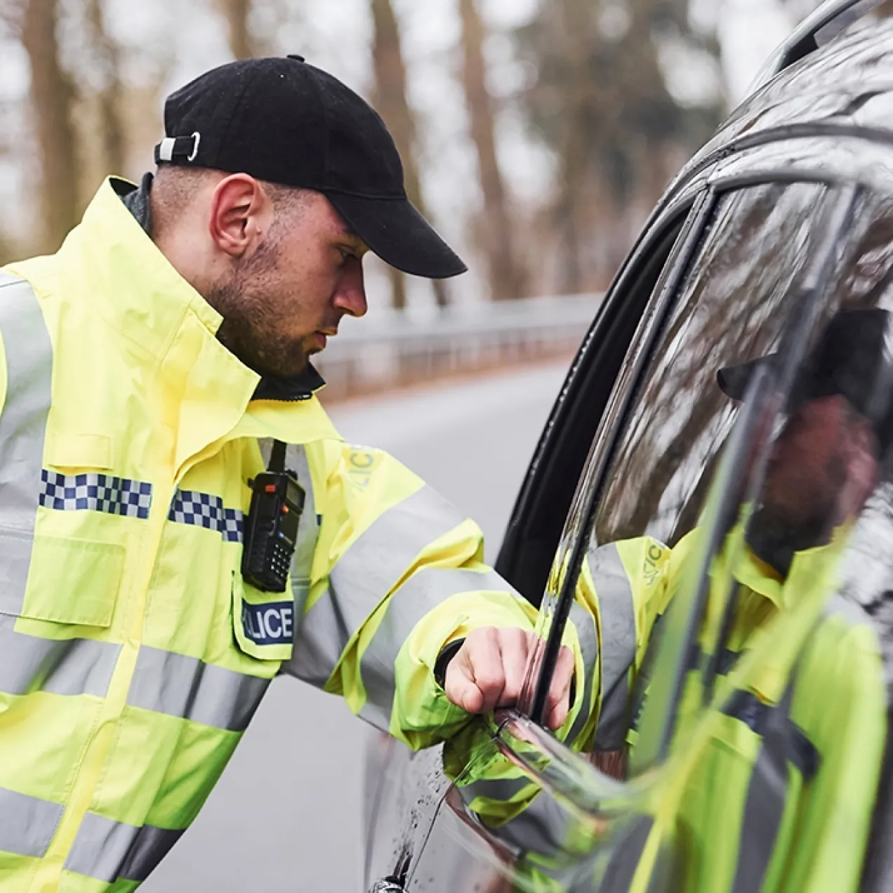 A Herzing University criminal justice graduate in a high-visibility police jacket conducts a routine traffic stop on a rural road.