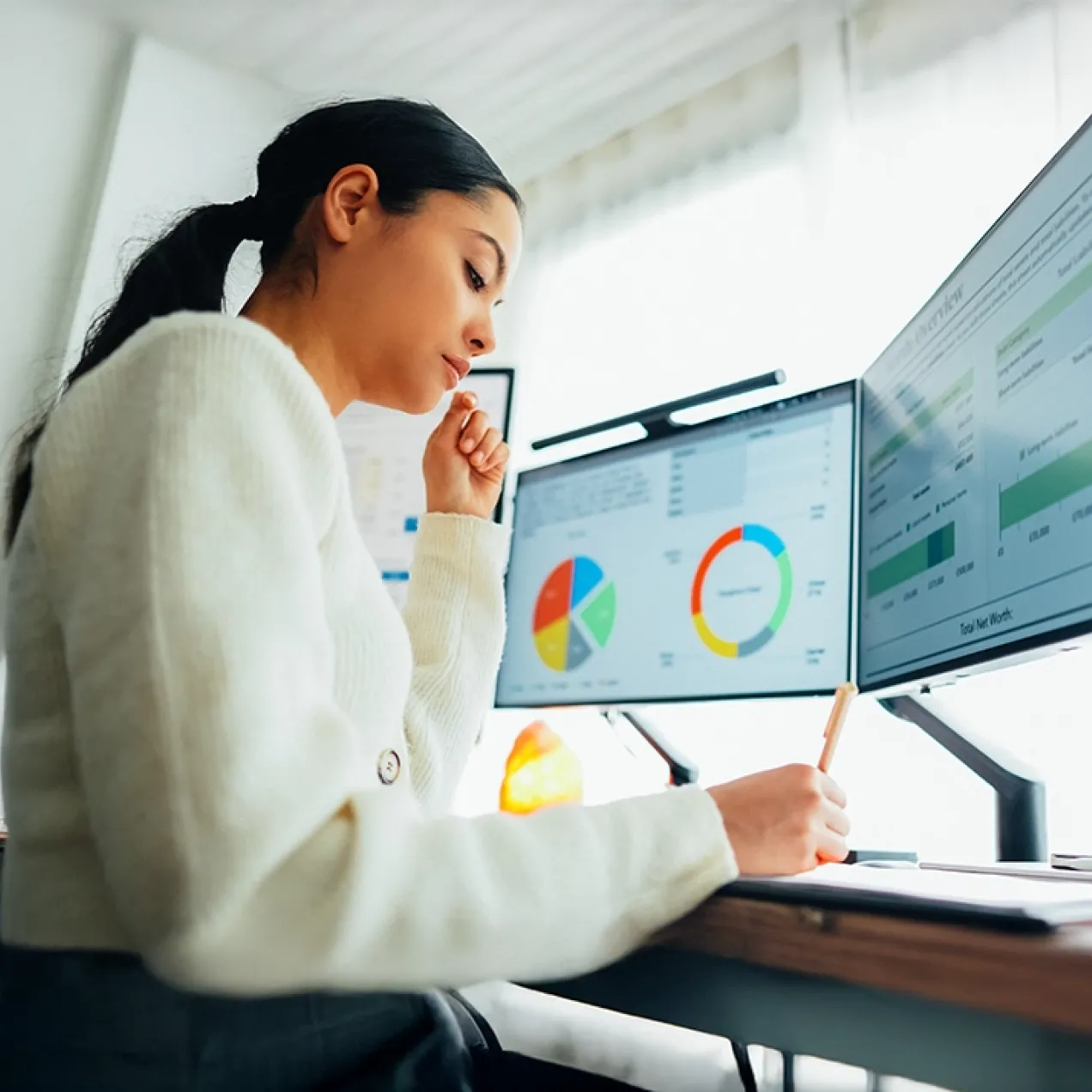 A professional woman analyzes data on dual monitors, representing the skills and expertise gained through Herzing University’s MBA in Business Analytics program.