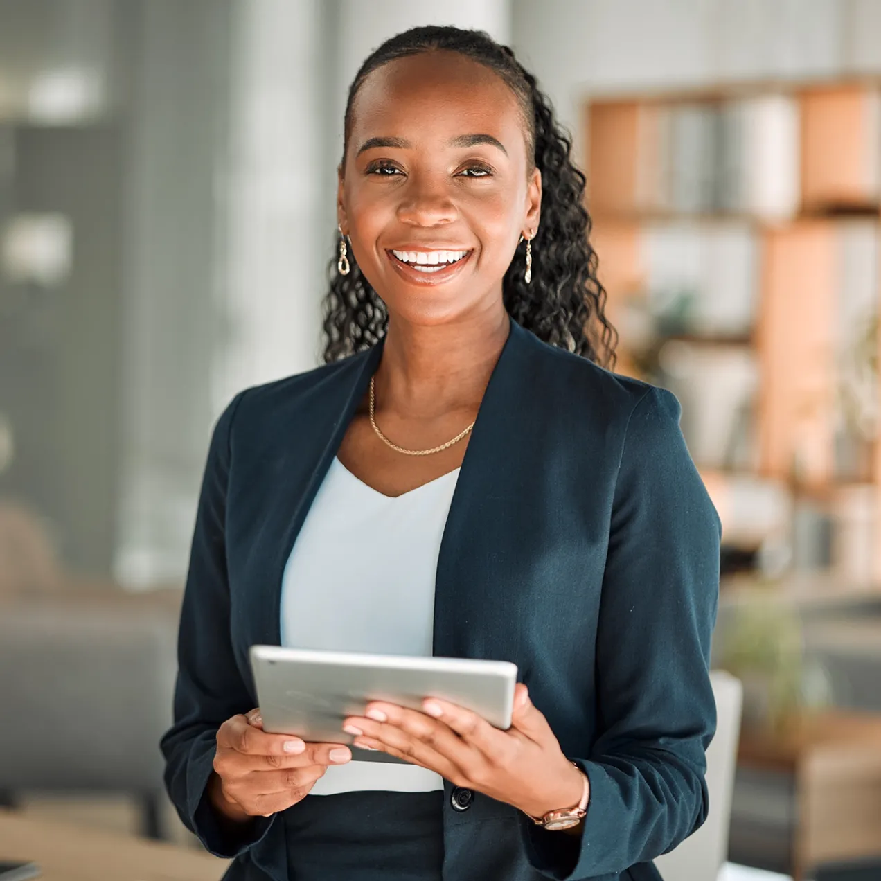 A smiling professional in business attire holds a tablet, representing career advancement opportunities with an MBA.