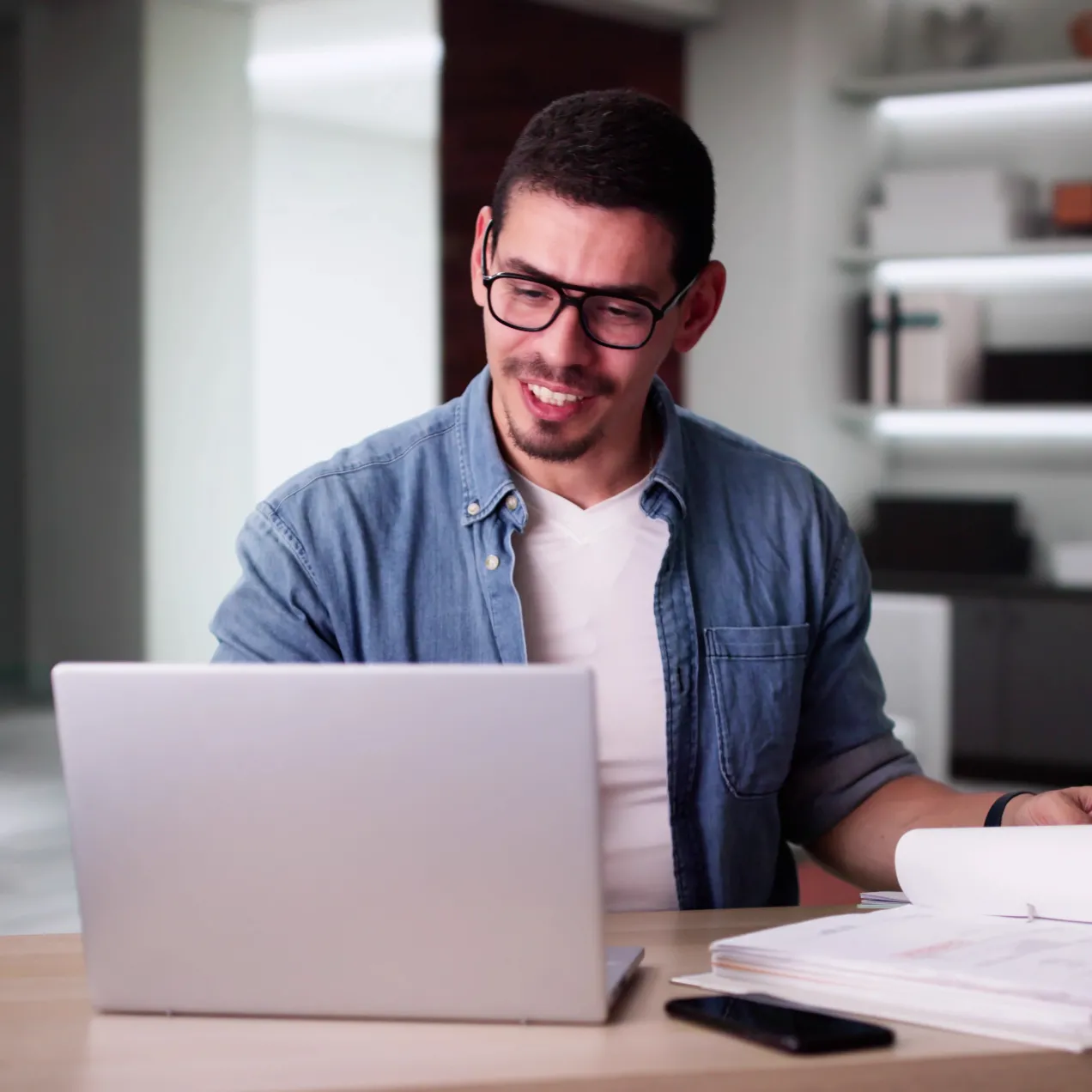 A man in a casual business setting studies financial documents and works on a laptop, representing career opportunities with a Herzing University accounting degree.