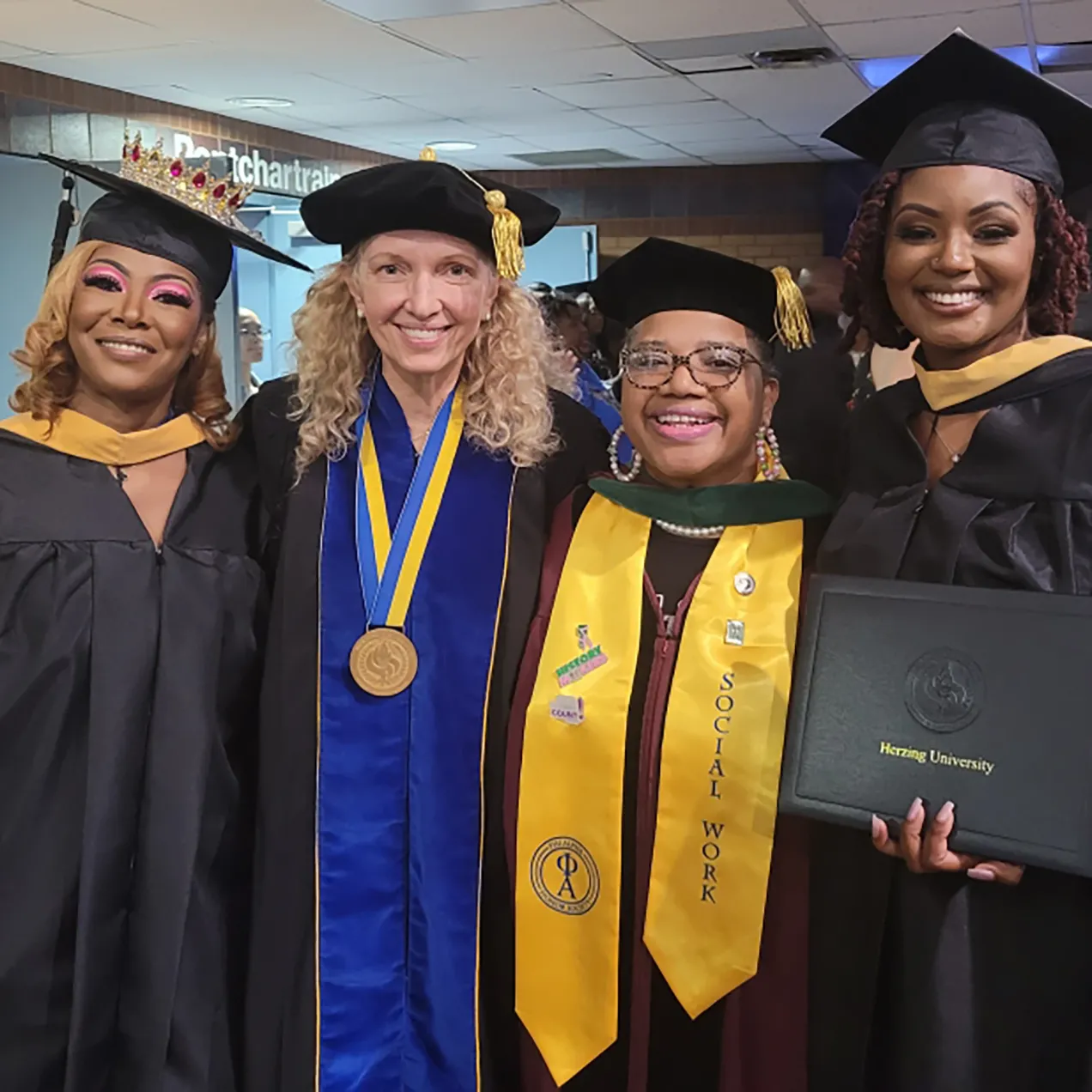 Group of smiling graduates and faculty at Herzing University commencement, with Social Work honor stoles and diploma proudly displayed.