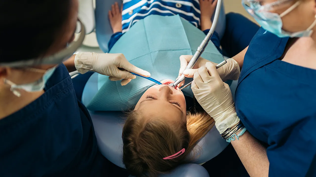 Dental assisting professionals performing a procedure on a young patient in a clinical setting, showcasing hands-on training in dental care.