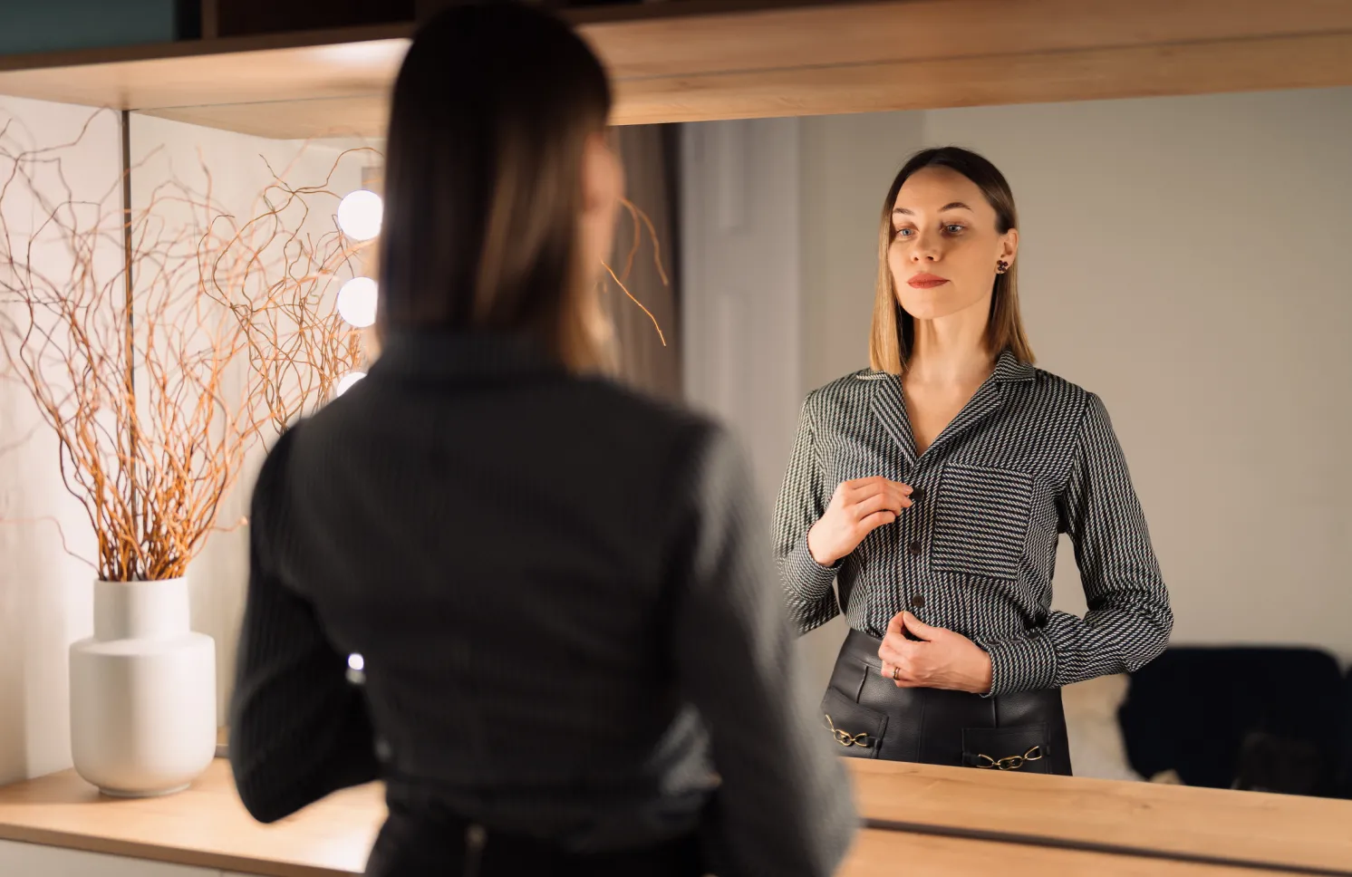 Self-confident woman looking at her reflection into the mirror indoors.