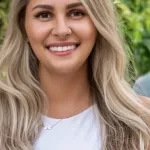 Blonde woman poses in front of foliage in a white shirt