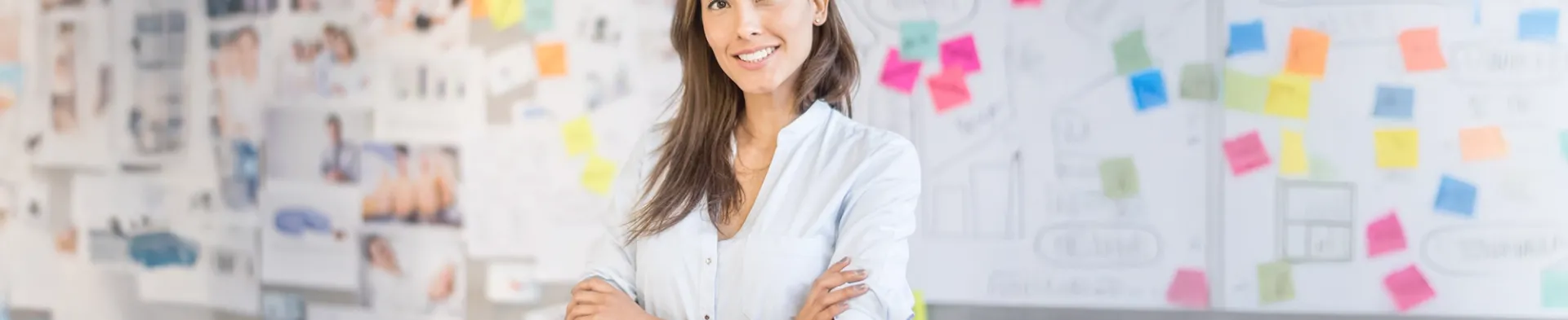 Smiling marketing professional standing in front of creative project board with colorful sticky notes