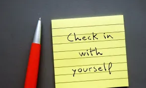 Note paper on gray background with handwritten text - Check in with yourself - carving out time each day to ask yourself how you're doing