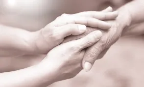 Caregiver, career hand holding elder hand in hospice care. 