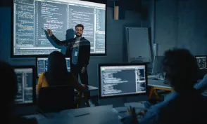 Teacher Giving Computer Science Lecture to Diverse Multiethnic Group of Female and Male Students in Dark College Room. Projecting Slideshow with Programming Code. Explaining Information Technology.