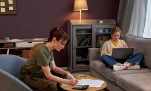 Side view portrait of young military woman working with documents at home, daughter in background, copy space