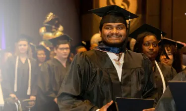 Herzing University online MBA graduate smiling while walking to receive his degree