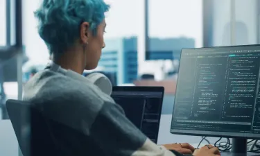 Application programmer seated in front of dual monitors in office environment coding