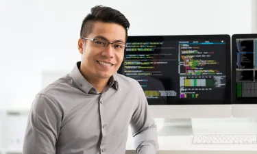 Computer programmer seated in front of two monitors showing coding software