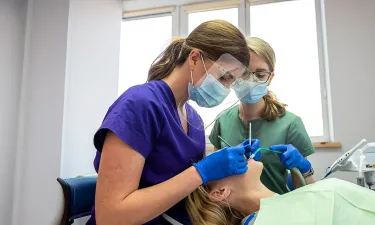 Two dental professionals in protective masks and gloves performing a procedure on a patient in a modern dental office, demonstrating teamwork and professionalism.