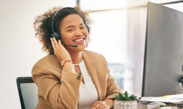 Professional woman in a headset smiling while working at a desk, representing a career in insurance billing and coding.