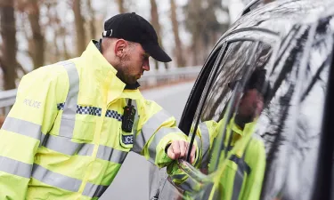 A Herzing University criminal justice graduate in a high-visibility police jacket conducts a routine traffic stop on a rural road.