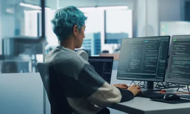 Application programmer seated in front of dual monitors in office environment coding