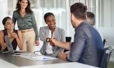 Human resources professional shaking hands with a candidate during a job interview in a modern office setting.