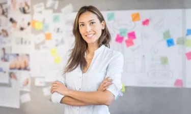 Smiling marketing professional standing in front of creative project board with colorful sticky notes