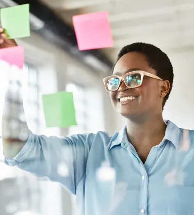 Smiling marketer placing colorful sticky notes on glass wall during brainstorming session