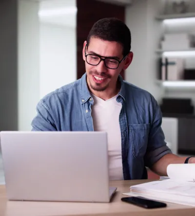 A man in a casual business setting studies financial documents and works on a laptop, representing career opportunities with a Herzing University accounting degree.