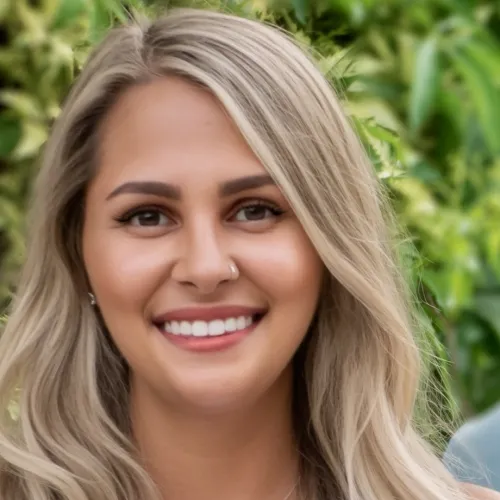 Blonde woman poses in front of foliage in a white shirt