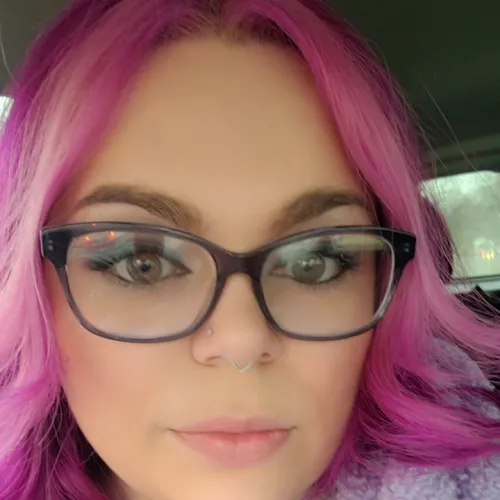 Woman with bright pink hair poses for a selfie in a car