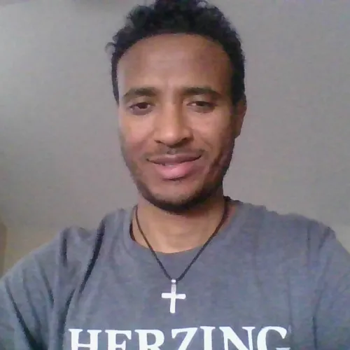 African American man in a Herzing shirt posing for a self in a bedroom