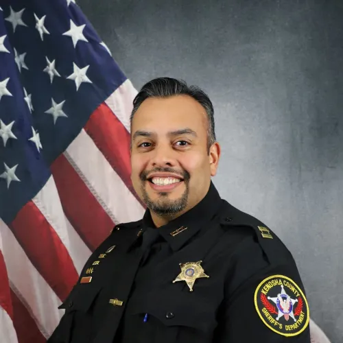 Tony Gonzalez in police uniform posing in front of an American flag