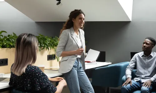 Group of diverse health and human services professionals engaged in a collaborative team meeting in a modern office setting, with one woman standing and speaking while others listen attentively