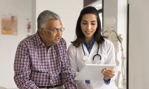 Older patient smiling while a nurse practitioner student reviews health information with him on a tablet Older patient smiling while an adult gerontology acute care nurse practitioner student reviews health information with him on a tablet