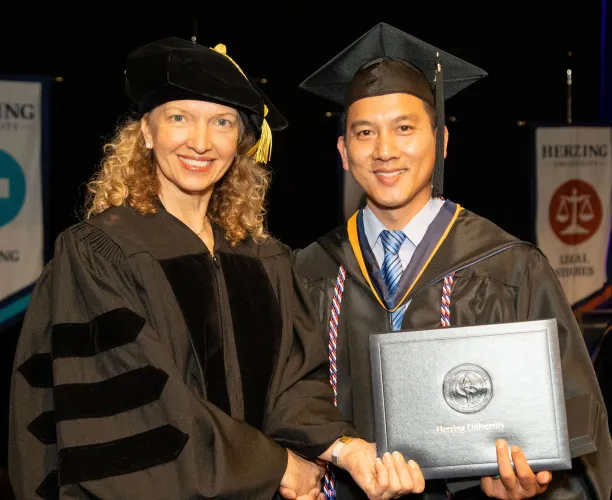 Herzing University graduation ceremony, professor shaking hands with a graduate holding their diploma.