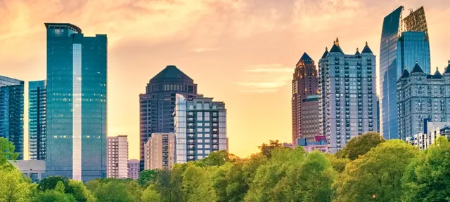 Panoramic view of the Atlanta skyline during sunset with modern skyscrapers and greenery in the foreground.