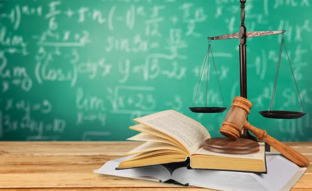 Gavel on books on a desk with scales and chalkboard in background