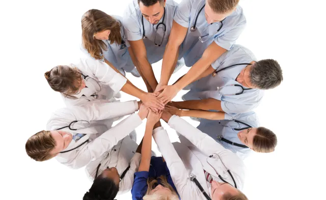 Group of medical professionals in a huddle with their hands stacked in the middle